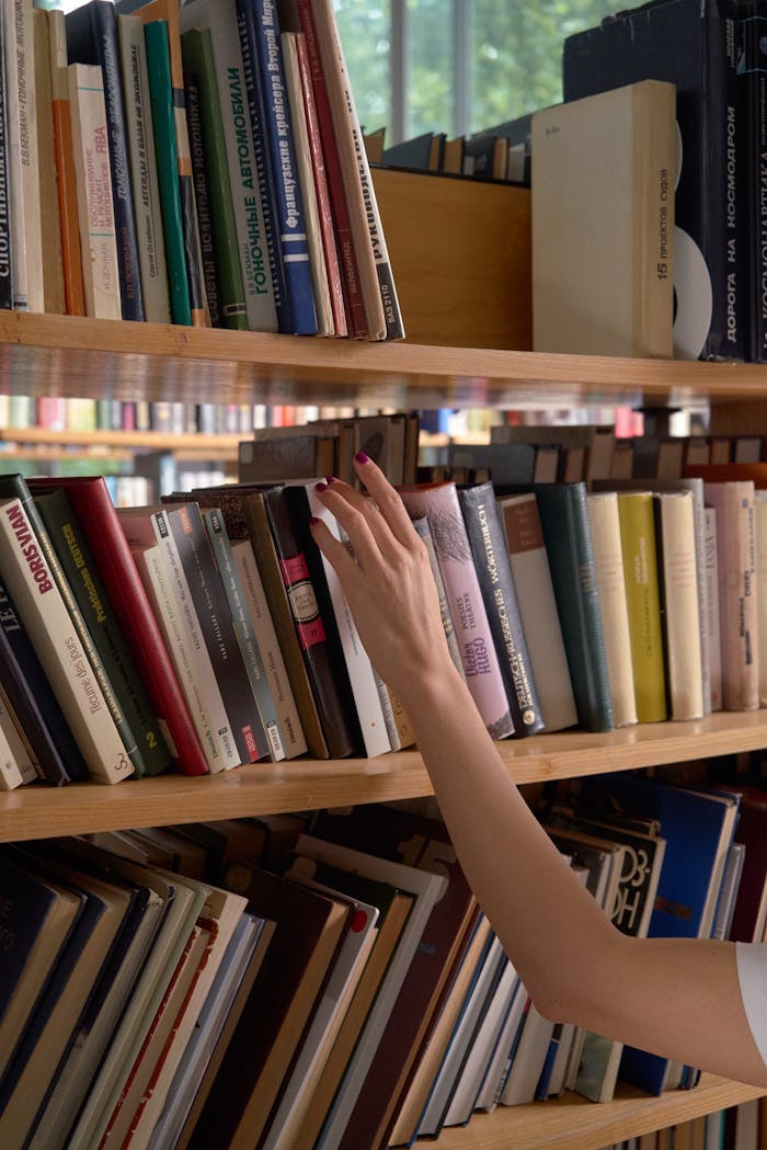 A hand reaching for a book on a library bookshelf, surrounded by diverse literature.